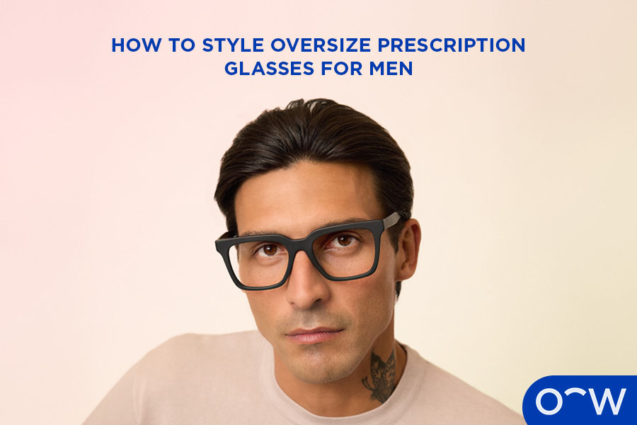 A man smiling at the camera wearing oversized square glasses.